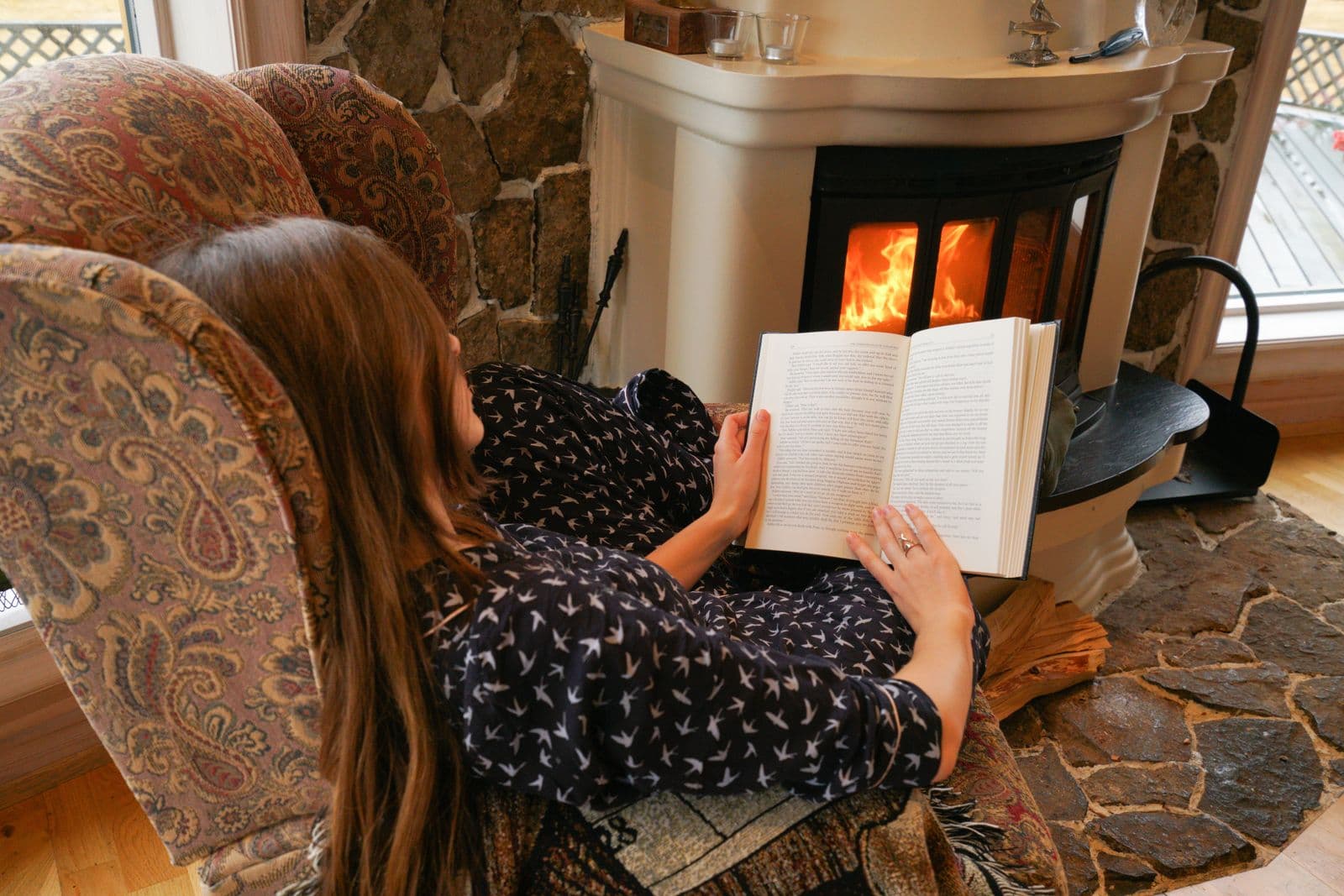 Personne lisant un livre, lovée dans un plaid près du feu
